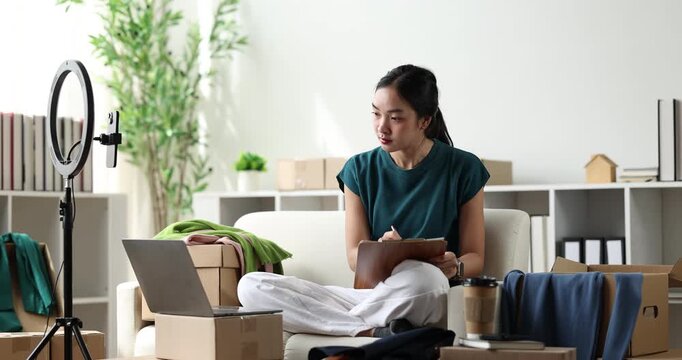 Asian woman streaming product review for online clothing business using a ring light