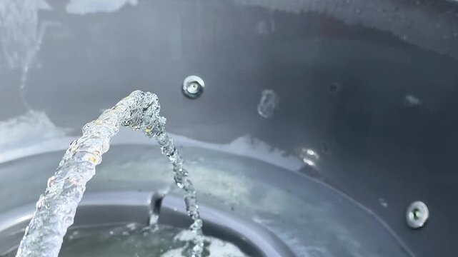 jacuzzi being cleaned with hose water stream, foam breaking down on plastic surface, jacuzzi interior washing process, outdoor maintenance activity, detail of sanitation, hygiene and care