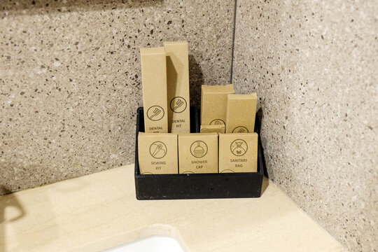 ollection of hotel amenities, including a dental kit, shower cap, sewing kit, and sanitary bag, neatly packaged in brown kraft paper boxes inside a black holder.