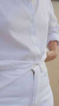 Close-up of a woman adjusting a white shirt and placing her hand in a pocket,