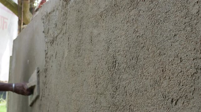 Construction worker smoothing concrete wall with plaster trowel