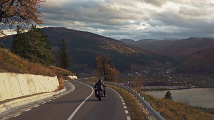 Fototapeta premium Motorcyclist riding winding mountain road enjoying scenic autumn landscape
