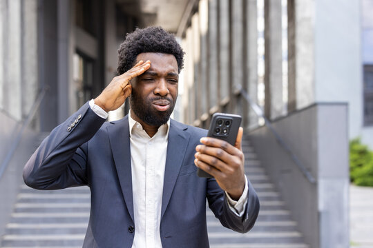 Unhappy businessman experiencing stress and frustration, holding a smartphone and reacting to upsetting information or a difficult situation outdoors