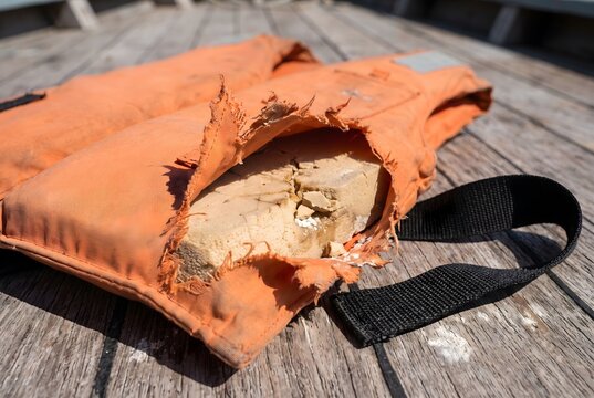 Close up of a torn nylon shell exposing damaged inner buoyancy foam on a life jacket laying flat on a boat deck