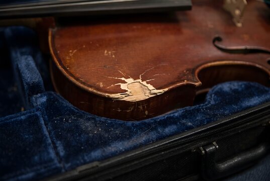 Close up of an impact dent and chipped varnish on the wooden surface of a violin inside a case