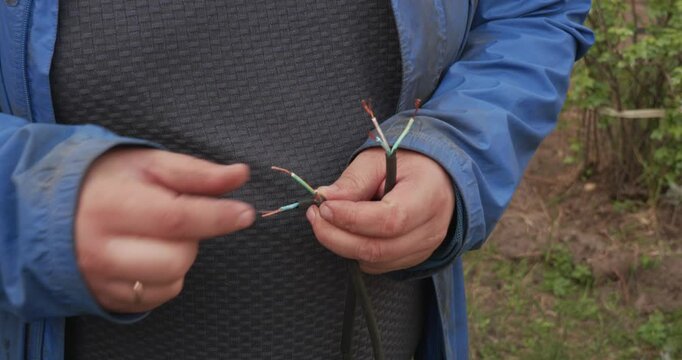 Close up view of an electrician's hands carefully wrapping red insulating tape around a damaged multicore electrical cable to repair and protect the exposed copper wiring outdoors.