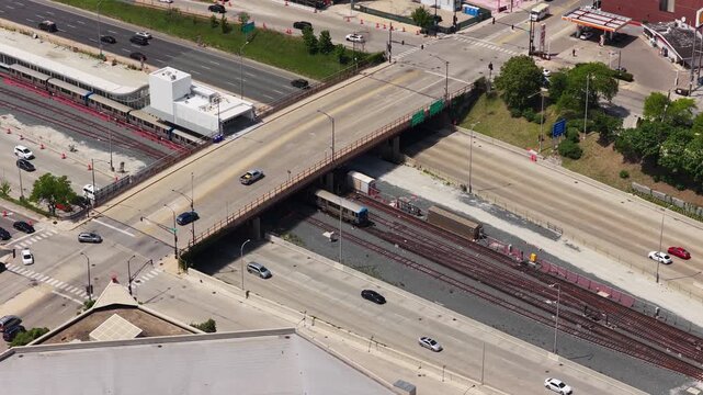 Metra train passing beneath overpass, elevated above Kennedy Expressway in urban Chicago, complex infrastructure and constant city traffic flow