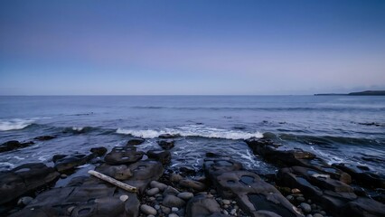 Fototapeta premium Calm ocean waves gently lapping against a rocky shoreline under a dusky sky