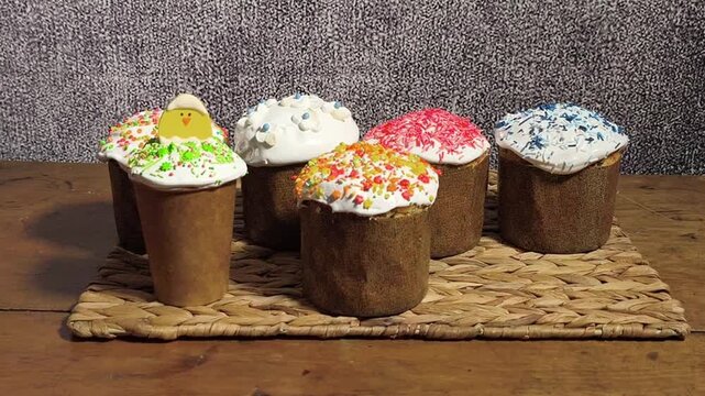 Group of glazed Easter cake treats arranged on rustic surface. Person holds delicious Easter cake with colorful sugar flowers. Seasonal religious bakery dessert and symbolic orthodox food.