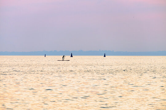 Silhouette of a paddleboarder on calm sea at sunset, peaceful waterscape with soft pastel sky and distant horizon in tranquil evening light