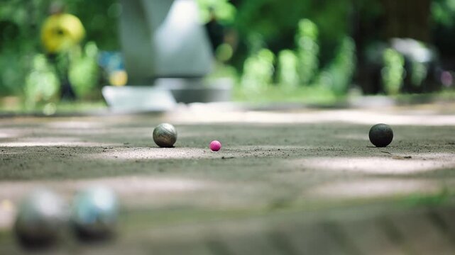 Players are playing petanque in a park on a sunny afternoon in an urban area