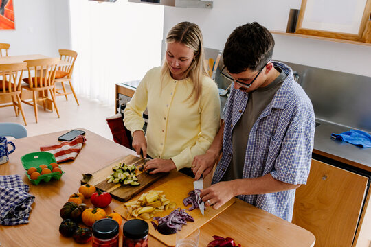 A couple works side by side, slicing vegetables at an island.