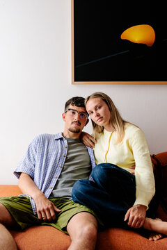 A smiling couple relaxes on an orange couch below a sunset print.