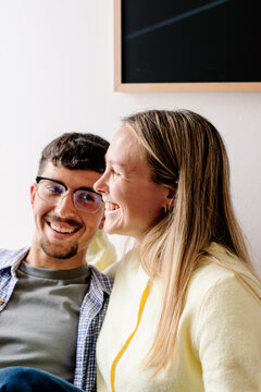 A happy couple laughs as a blonde woman embraces the man from behind.