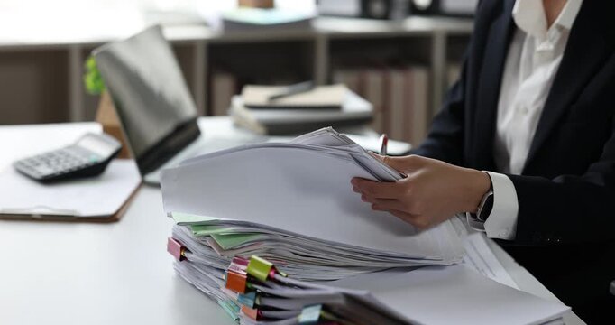 Professional businesswoman organizing a large stack of documents, highlighting a busy office workload