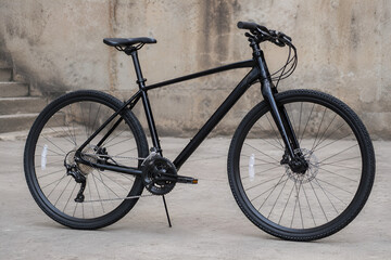 Fototapeta premium Minimalist Matte Black Hybrid Bicycle with Disc Brakes Parked Against an Urban Concrete Wall in Modern Lifestyle Style