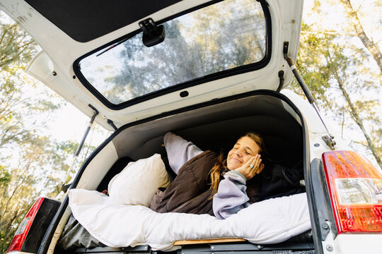 Woman welcoming from campervan bed in cozy autumn forest campsite