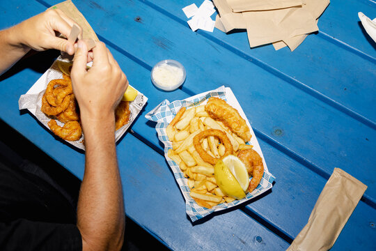 Anonymous person eating fish and chips at blue picnic table