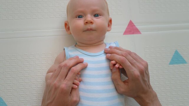 Father gently stroking baby son's chest on soft mat. Close-up. Slow motion.
