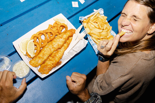Woman laughing while eating chips with fish and chips on blue table