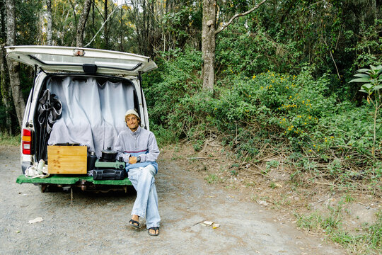 Man sitting in open campervan with camp stove and forest backdrop