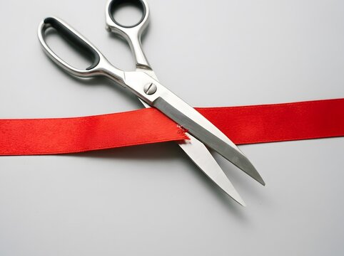 Pair of sharp metal scissors cutting through bright red decorative ribbon
