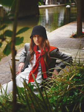Stylish Woman Sits by the Water in Urban Area With Greenery
