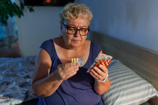 Senior overweight lady wearing glasses holding medication pills in room.