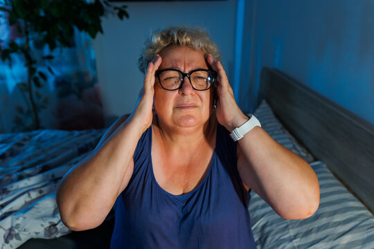 Older woman holding temples suffering severe headache late at night.