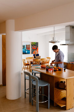 A man preps food while a smiling woman sits with her laptop.