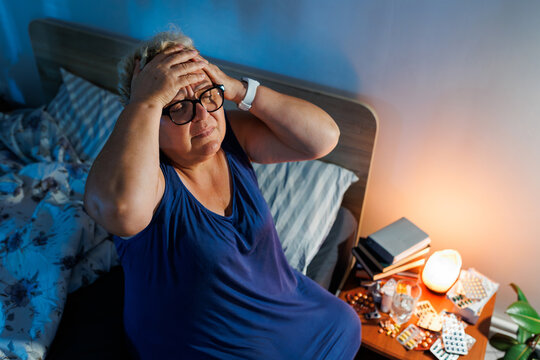 Older woman suffering terrible headache near medical pills late at night.
