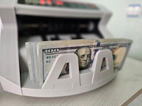 Counting money in a bill counter with several 100 dollar bills in a bank