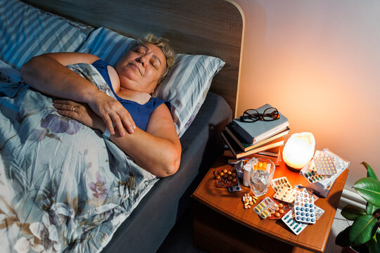 Senior lady resting in dark bedroom near medical pills late at night.