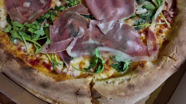 a top-down view of sliced pizza with prosciutto and greens on a wooden surface, showcasing the delicious and appetizing appearance of the dish in a kitchen or dining area, with brown.