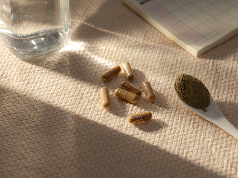 Herbal supplements and powder on a textured surface with a glass