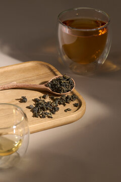 Loose leaf oolong tea on a wooden spoon and tray with brewed tea