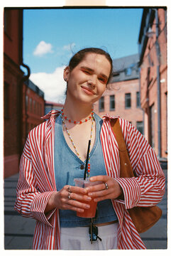 Young woman holds a drink while walking in a city street
