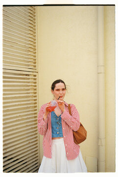Young woman enjoys a soft drink while standing against a wall