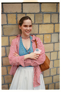 Smiling Woman stands against a brick wall wearing a striped shirt