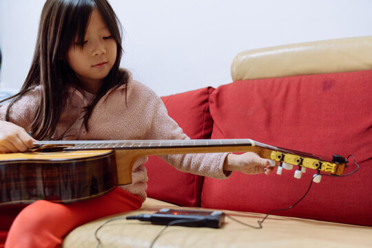 Young Girl Tunes Guitar While Sitting on Sofa in Living Room