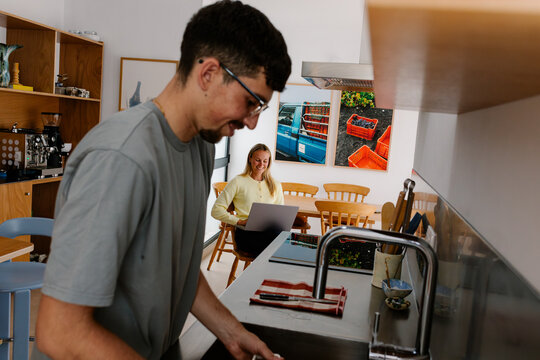 A man works at the counter while a woman uses a laptop nearby.