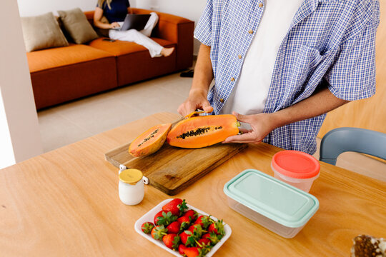 A fit man dices fresh papaya on a calm morning at home.