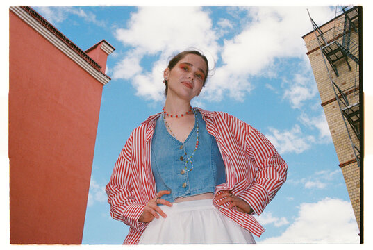 Woman poses in bright outfit against colorful buildings and sky