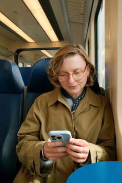 Happy woman on a train looking at her mobile phone, scrolling