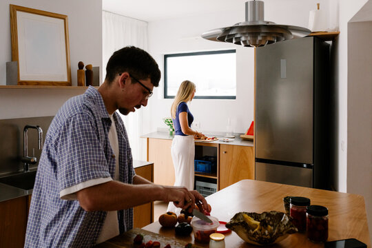 A man chops ingredients while a woman prepares food in the kitchen.