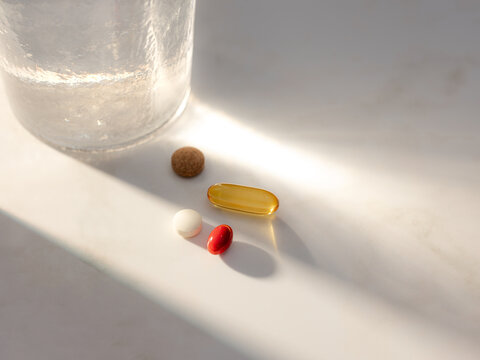 Various pills and a glass of water on a white surface with soft light
