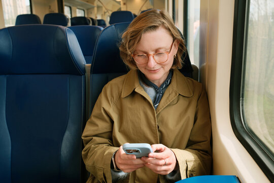 Happy smiling woman on a train looking at her smartphone, scrolling