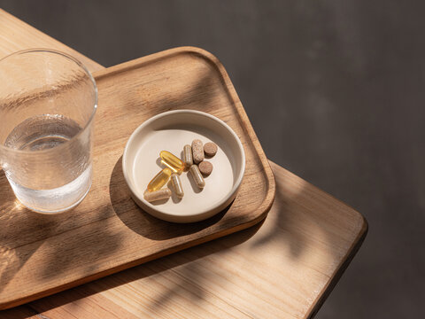 Daily health supplements and a glass of water on a wooden tray