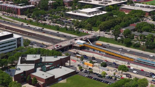 Aerial shot of Chicago L Train at a station with heavy traffic on the Dan Ryan Expressway alongside lush urban neighborhood during a sunny summer afternoon