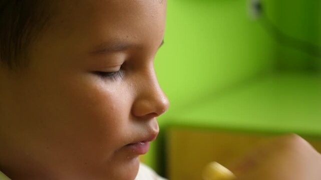 Boy enjoys eating sweet corn puffs at home, savoring every bite. Close up portrait of his face in natural indoor light.